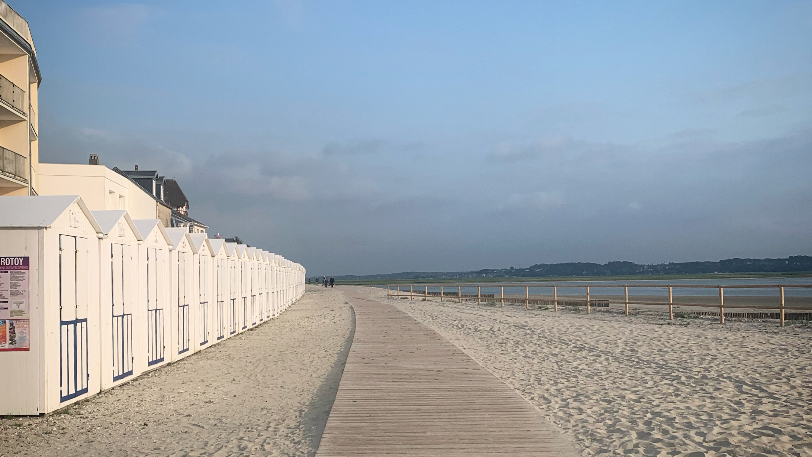 A woodend slatted footpath and a row of white beach huts on the white sands of the bay of the Somme